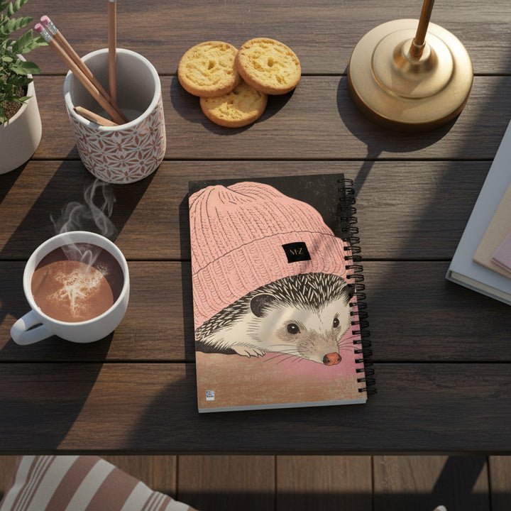 Photographie professionnelle lifestyle,  beau carnet A5 Mzelle design motif herisson, entre une tasse de chocolat chaud, des biscuits sablés, un porte-crayons en céramique, coussins rayés décoratifs au sol de bois sombre.