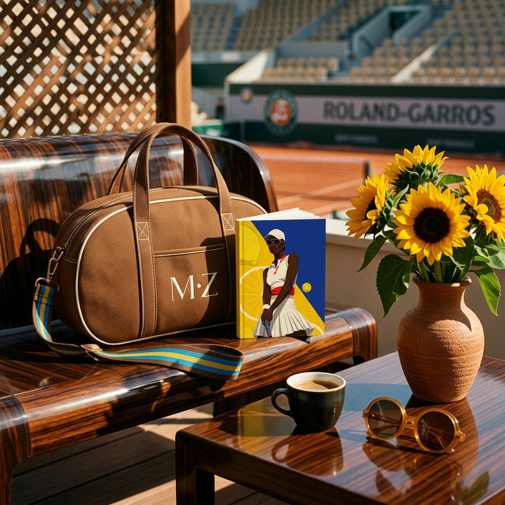 Photographie d'extérieur esprit sport, inspiré des cours de Roland Garros, superbe Sac de sport de forme ovale,  point focal sur le carnet mzelle design illustré d'une joueuse de tennis, posé à côté du sac , sur une table basse un bouquet de tournesols, et des lunettes de soleil 70's, et 1 café, lumière franche. 