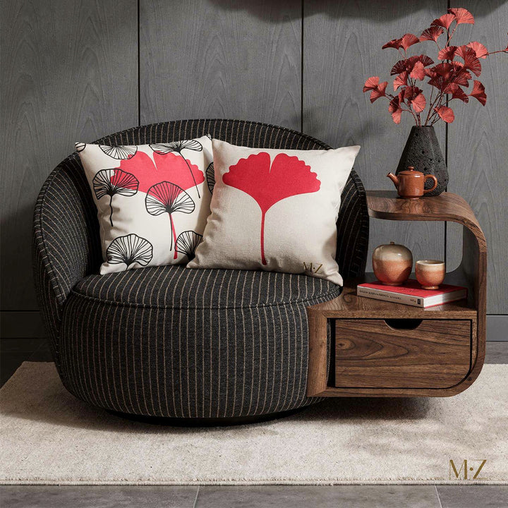 Photographie  d'un large fauteuil en forme d'ovale moderne, assise en coton noir finement rayé de beige, orné de deux coussins mzelle design motifs ginkgo graphique rouge et noir. Un côté du fauteuil servant de table basse, avec un tiroir peint d'un motif en écaille de poisson noir et beige. Service à thé en céramique.