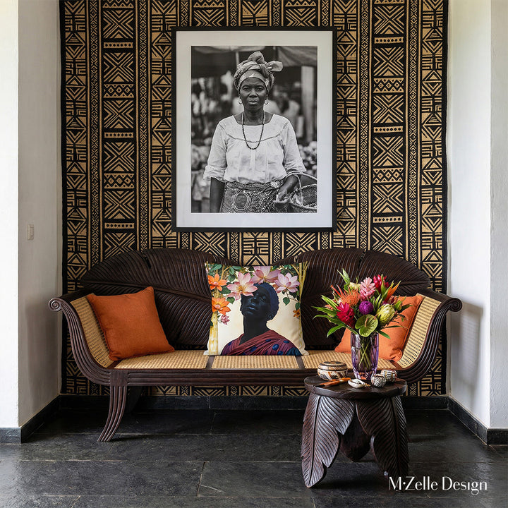 Photographie d'une villa créole d'architecte, un canapé créole au dossier en forme de feuille de bananier en bois wengé et assise en cannage, orné de coussins, placé contre un mur avec un tissu mural à motif tribal. 