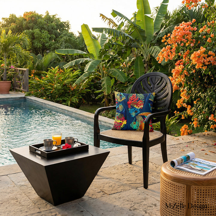Photographie lifestyle professionnelle, villa créole d'exception nichée au cœur d'un jardin tropical, bananiers et bougainvilliers orange,  vue de la piscine et de deux sublimes fauteuils en ébène au design moderne, dossier arrondi sculpté en forme de feuille de monstera, assise en cannage beige finement travaillée, chacun orné d'un grand coussin motifs poissons.