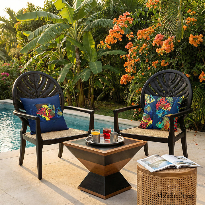 Photographie lifestyle professionnelle, villa créole d'exception nichée au cœur d'un jardin tropical, bananiers et bougainvilliers orange,  vue de la piscine et de deux sublimes fauteuils en ébène au design moderne, dossier arrondi sculpté en forme de feuille de monstera, assise en cannage beige finement travaillée, chacun orné d'un grand coussin motifs poissons.