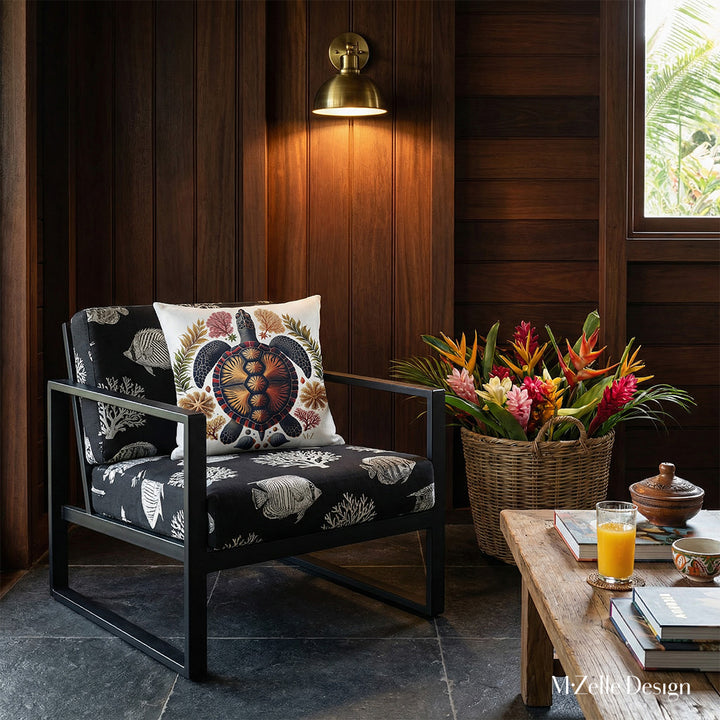 Photographie intérieure de style éditorial d’une villa créole d'architecte, vue de face d'un fauteuil en lin noir, avec des motif blanc représentant des poissons tropicaux et des coraux, orné d'un coussin carré motif tortue, placé contre un mur de panneaux de bois sombre.