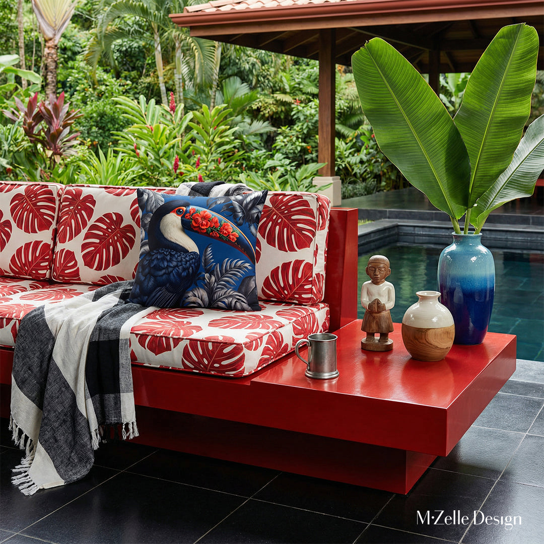 Photographie professionnelle extrêmement détaillée esprit estival, vue de face en gros plan sur un canapé en bois peint rouge laqué, structure épaisse épurée qui comporte une extension pour faire une table basse intégrée, assises à motifs monstera rouge et blanc, orné d'un grand coussin motif toucan bleu,  exposé sur la véranda.