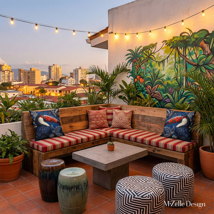 Photo professionnelle lifestyle d'une terrasse de bar au costa rica, au crépuscule vue sur la ville, espace moderne et éclectique, avec un  banc d'angle en forme de L rouge et beige orné de coussins rayés et de chaque coté se trouve 2 larges coussins motif toucan MZele Design.