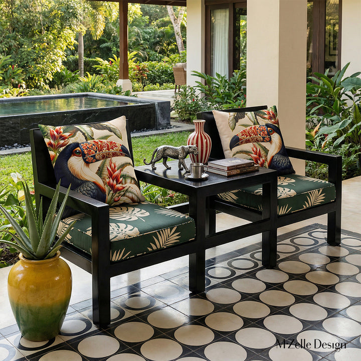 Photographie professionnelle Décoration d'intérieur extrêmement détaillée vue de face sur 2 fauteuils en bois peint noir laqué, structure épaisse reliés entre eux par une table basse intégrée, assises vert foncé à motifs graphiques de feuilles tropicales ecrus, orné de 2 grands coussins motifs toucans.