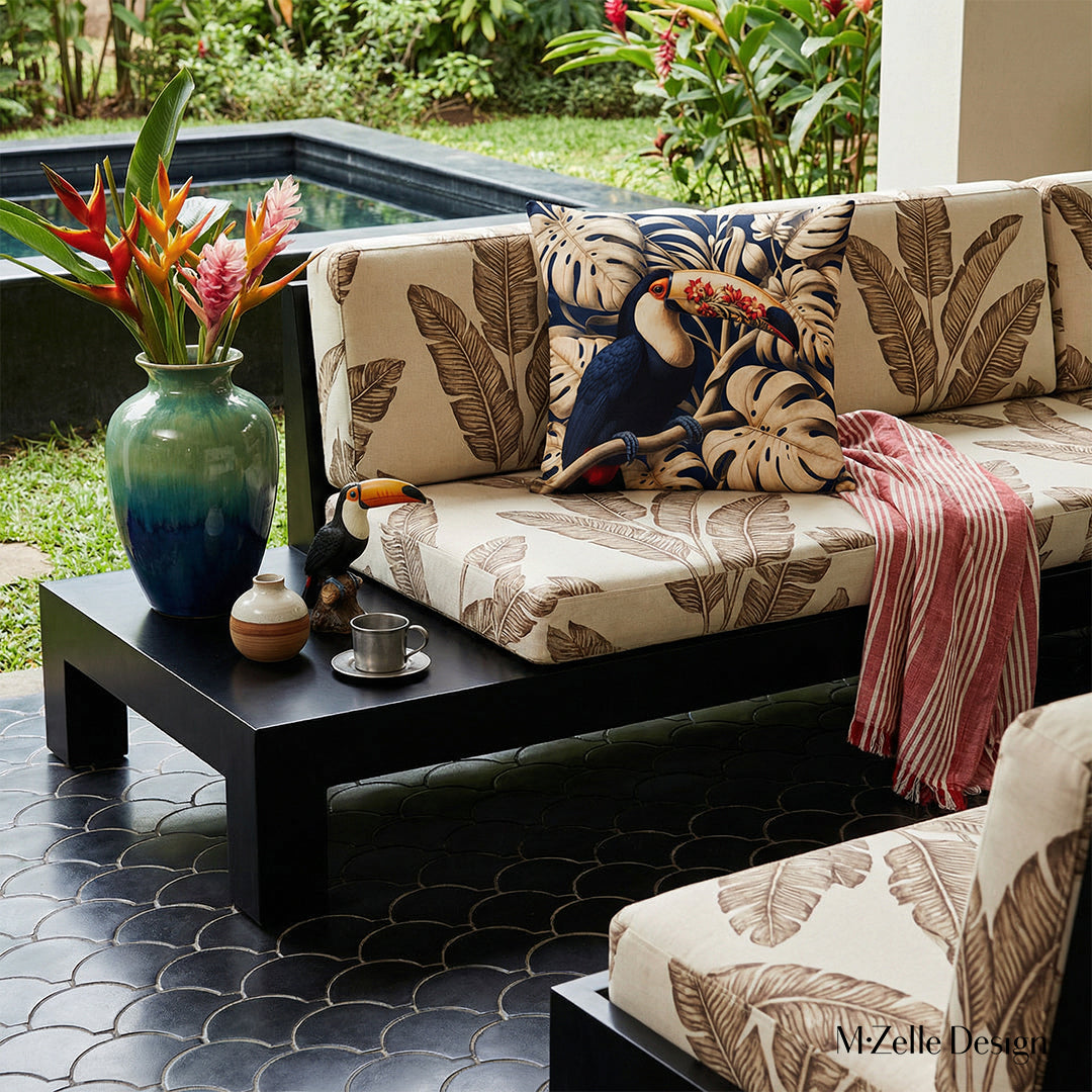Photographie professionnelle extrêmement détaillée esprit estival, vue de face en gros plan sur un canapé en bois peint noir laqué, structure épaisse épurée qui comporte une extension pour faire une table basse intégrée, assises écrues à motifs graphiques de feuille de bananier marron, orné d'un grand coussin , exposé sur la véranda.