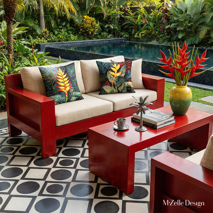 Photographie professionnelle extrêmement détaillée d'esprit estival, vue de face en gros plan sur un canapé en bois peint rouge laqué, structure épaisse et une table basse,  me canapé est orné de deux grands coussins motifs héliconias mzelle design, piscine et végétation en arrièreplan.