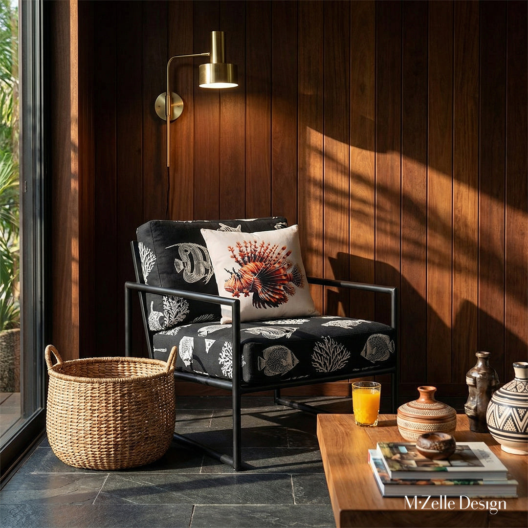 Photographie intérieure de style éditorial d’une villa créole d'architecte,  fauteuil épuré en métal noir et  lin noir, avec des motif blanc représentant des poissons tropicaux et des coraux, orné d'un coussin carré motif poisson lion, panneaux de bois au mur.
