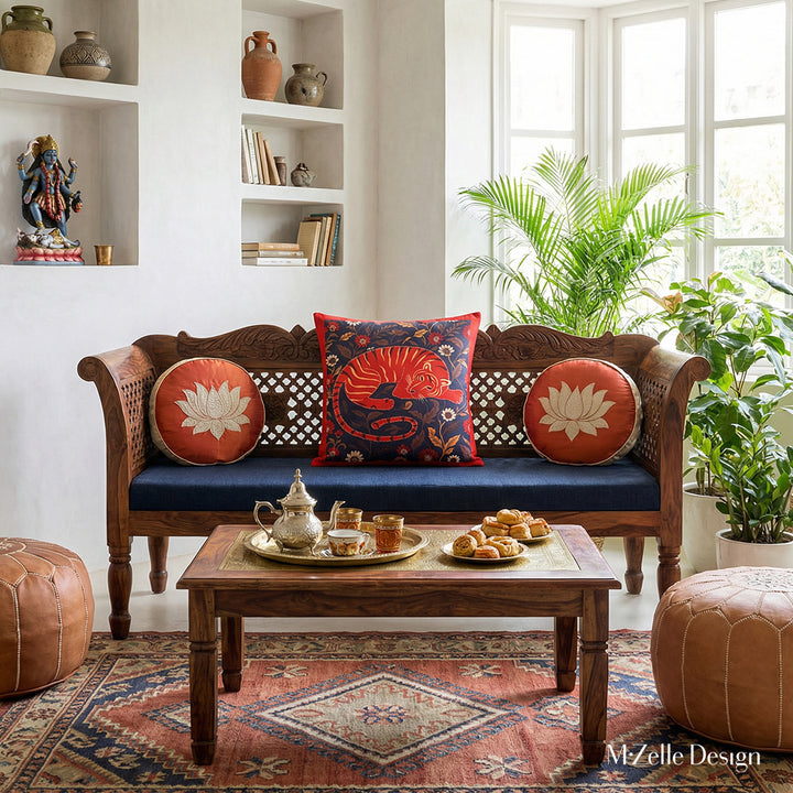 Photographie professionnelle extrêmement détaillée , Villa Riad lumineuse mélange de style nomade berbère et Inde du Sud, vue de face d'un superbe banc, assises de tissu écru orné d'un large coussin carré motifs indiens mzelle design et de 2 coussins ronds en soie rouges avec un lotus brodé ecru, service à thé marocain et pâtisseries orientales sur la table basse sheesham sculptée.