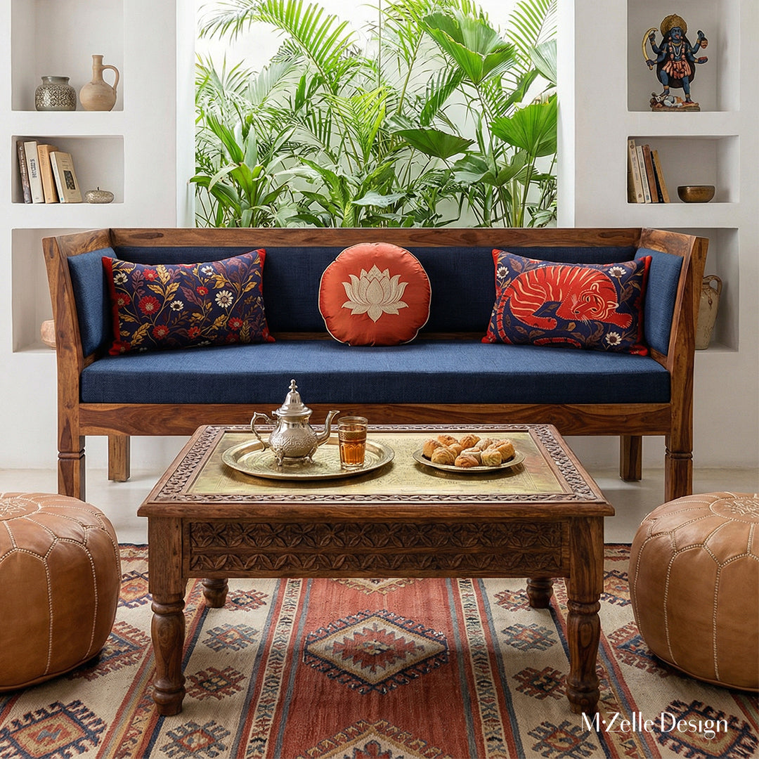 Photographie professionnelle extrêmement détaillée , Villa Riad lumineuse mélange de style nomade berbère et Inde du Sud, vue de face d'un superbe banc, assises de tissu écru orné de 2coussins rectangles motifs indiens mzelle design et de 2 coussins ronds en soie bleu nuit avec un lotus brodé rouge, service à thé marocain et pâtisseries orientales sur la table basse sheesham sculptée.