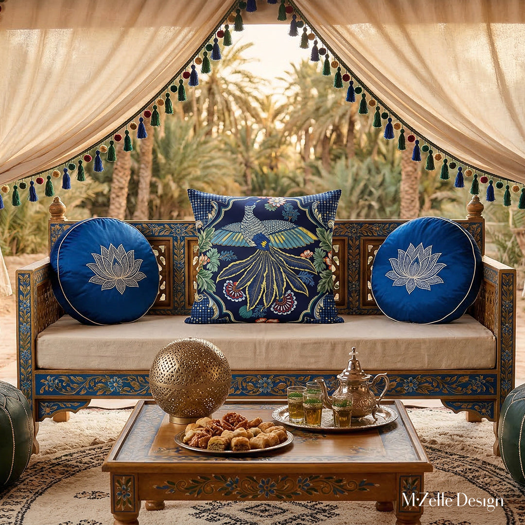 Photographie professionnelle de décoration de tente nomade d'inspiration Indo-berbère, superbe banquette Style dravidien, en bois de manguier peint à la main orné de large coussin motif oiseau mzelle design au centre, et un coussin rond en lin brodé , une table en bois de manguier peint à la main : une lampe sphérique ajourée, un service de thé à la menthe et des pâtisseries orientales