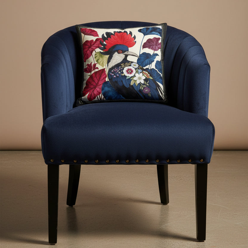 Photographie professionnelle qualité studio, d'un coussin mzelle design disposé sur une chaise crapaud en velours bleu nuit, rivet en laiton, dossier arrondi matelassé, sans accoudoirs, disposée dans un décor neutre beige, sol ciment.