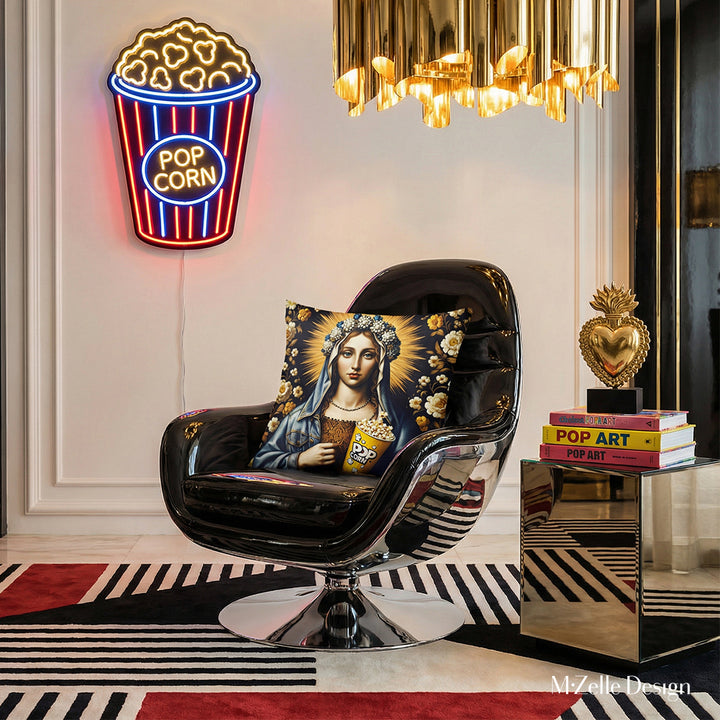 Photographie professionnelle lifestyle,  d'un salon lumineux, vue de face d'un fauteuil noir au design futuriste orné d'un large coussin motif vierge marie , autres éléments de décoration comme un tapis, un chandelier, des livres, au mur un pot de pop corn en néon, ex voto et tapis graphique.