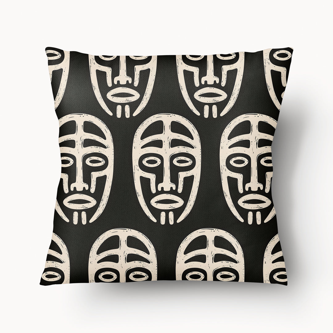 Coussin graphique de décoration de la marque MZelle Design, sur fond noir un motif beige représente un all over de masque tribal, style rupestre moderne