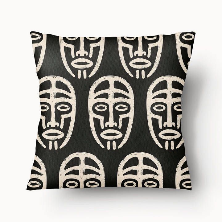Coussin graphique de décoration de la marque MZelle Design, sur fond noir un motif beige représente un all over de masque tribal, style rupestre moderne