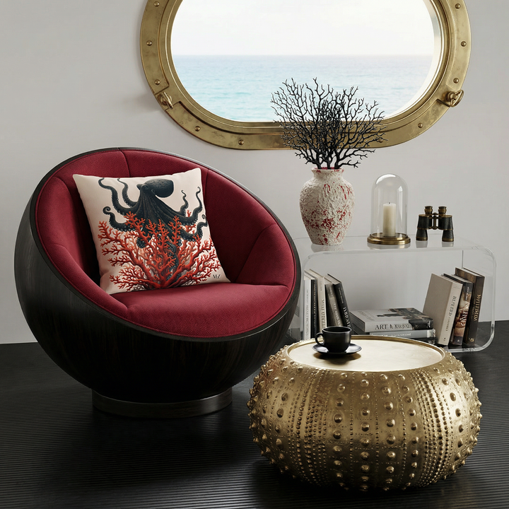 Photo professionnelle de décoration d'intérieur de villa côtière aux Bahamas, mettant en avant un superbe fauteuil sphérique en bois d'ébène, et tissu  rouge carmin foncé, orné d'un large coussin mzelle design motif  pieuvre artistique et corail rouge, table basse  en forme d'oursin en laiton, avec tasse de café noire posée dessus. 
