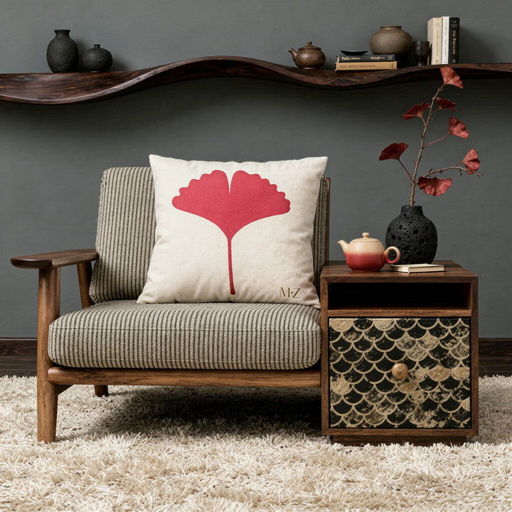 Photographie d'intérieur décoration style japandi-nordique, épuré mais chaleureux, fauteuil-futon moderne assise en lin finement rayé noir et beige orné d'un large coussin mzelle design motif ginkgo graphique, table en bois sur un côté du fauteuil avec un tiroir peint d'un motif en écaille de poisson noir et beige. Service à thé en céramique et vase en pierre noire.