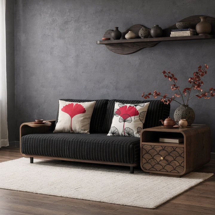 Photographie d'intérieur décoration  japandi-nordique, épurée mais chaleureux, douce lumière naturelle. Vue de face d'un fauteuil-futon moderne assise en lin finement rayé noir et beige orné de deux larges coussins mzelle design,  table basse avec un tiroir peint d'un motif en écaille de poisson noir et beige. Service à thé en céramique et branches de gonkgo.