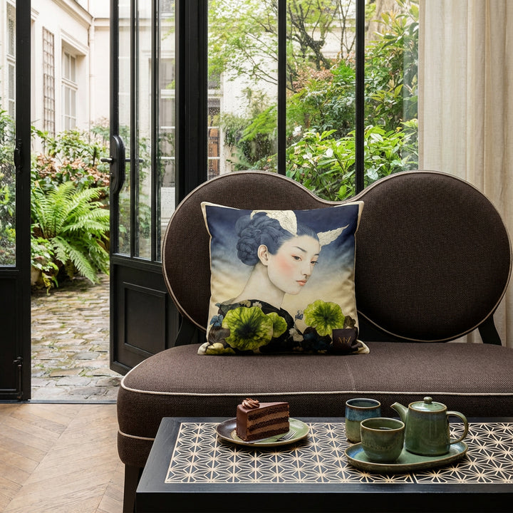 Photographie de décoration salon de thé, petite banquette ornée d'un large coussin carré mzelle design motif geisha au centre, sur une table de bistrot en bois peint noir mat avec des motifs japonais asanoha écrus minutieux, parts de layer cake au chocolat, service à thé en grès vert et bleu, en arrière plan une verrière. 