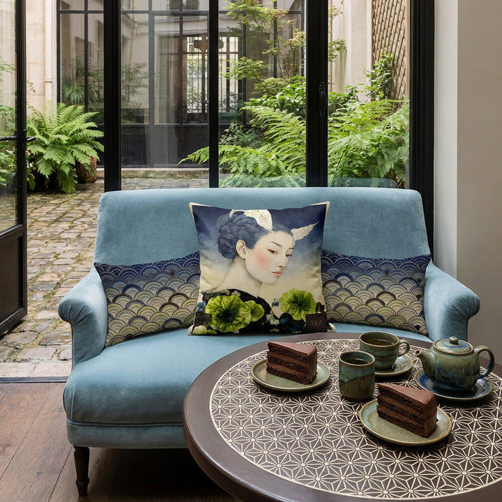 Photographie de décoration salon de thé, petite banquette bleu glacier, orné d'un large coussin carré mzelle design motif geisha au centre, sur une table de bistrot en bois peint noir mat avec des motifs japonais asanoha écrus minutieux, parts de layer cake au chocolat, service à thé en grès vert et bleu, en arrière plan une verrière. 