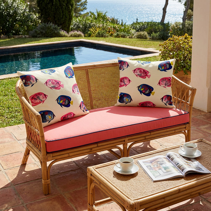 Photo professionnelle de décoration villa provençale, baignée de soleil , banquette 2 places au design moderne en bambou tressée , assises rose corail,  ornée de chaque côté d'un large coussin motif poissons tropicaux mzelle design , carrelage tomette au sol, table basse en bambou tressé. 