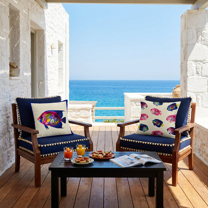 Photo professionnelle de décoration d'une villa méditerranéenne, murs blanchis, baignée de soleil, deux fauteuils en bois foncé , assises bleu marine finitions pompons écrus, chacun orné d'un large coussin mzelle design motifs poissons tropicaux ,  table basse en bois noir, verres de jus de fruits, tapas, et un magazine , en arrière plan vue sur la mer. Atmosphère invitante et haut de gamme.