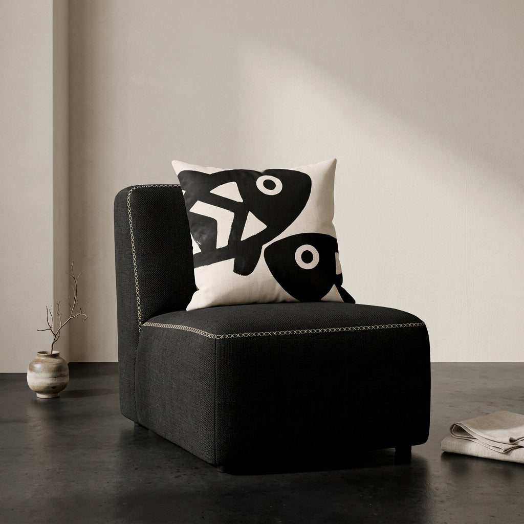 Photographie professionnelle qualité studio, d'un coussin carré mzelle dsign motifs poissons disposé sur une chaise japonaise sans accoudoirs, dossier en tissu noir surpiqué de fil écru, structure épaisse, disposé dans décor écru neutre, sol en béton ciré noir.