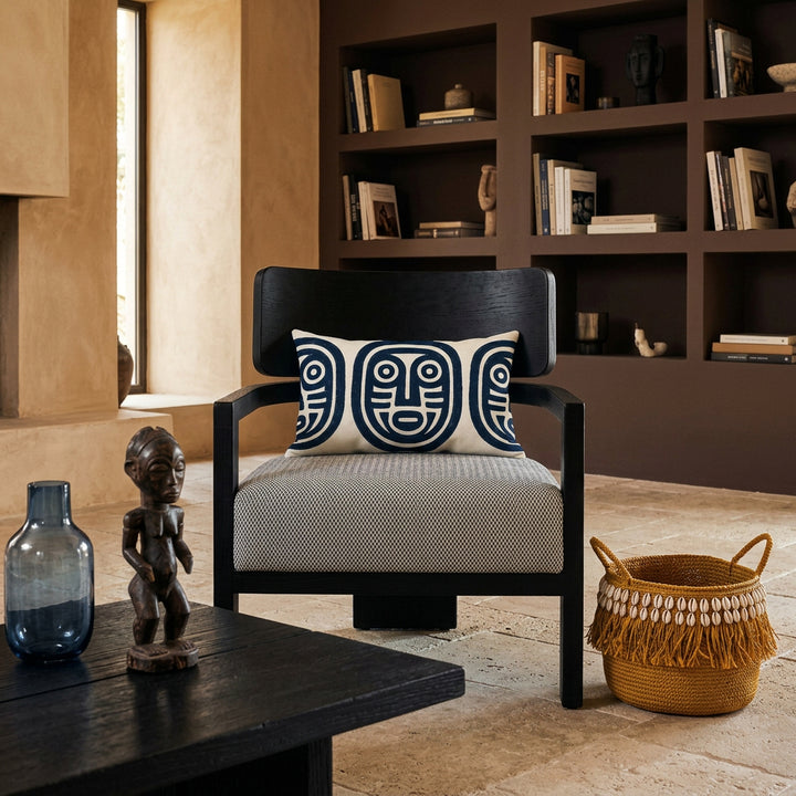 Photo professionnelle lifestyle, décoration Salon ethno-créole haut de gamme, chaise au design audacieux vue de face,  ornée d'un coussin rectangulaire mzelle design. Table basse en bois brûlé noir garni d'un vase en verre fumé bleu et d'une statuette style vaudou artistique.