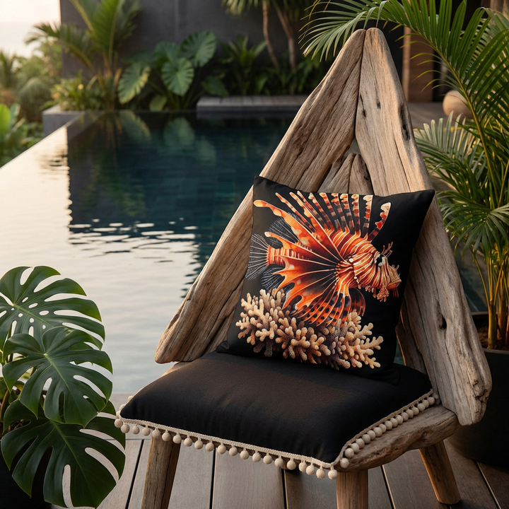 Photographie professionnelle d'un grand coussin mzelle design motif poisson lion et corail, disposé sur une chaise au design original et contemporain en bois flotté, triangulaire, assise noire finitions petits pompons écrus, placé devant une piscine sombre moderne à débordement et plantes exotiques.