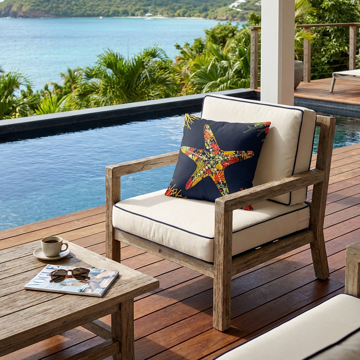 Photo professionnelle de décoration d'une terrasse de villa créole baignée de soleil , vue de droite d'un fauteuil en bois flotté au design simple , assises en tissu écru piping bleu marine , orné d'un large coussin à motif étoile de mer mzelle design, placé devant une piscine sombre moderne à débordement.