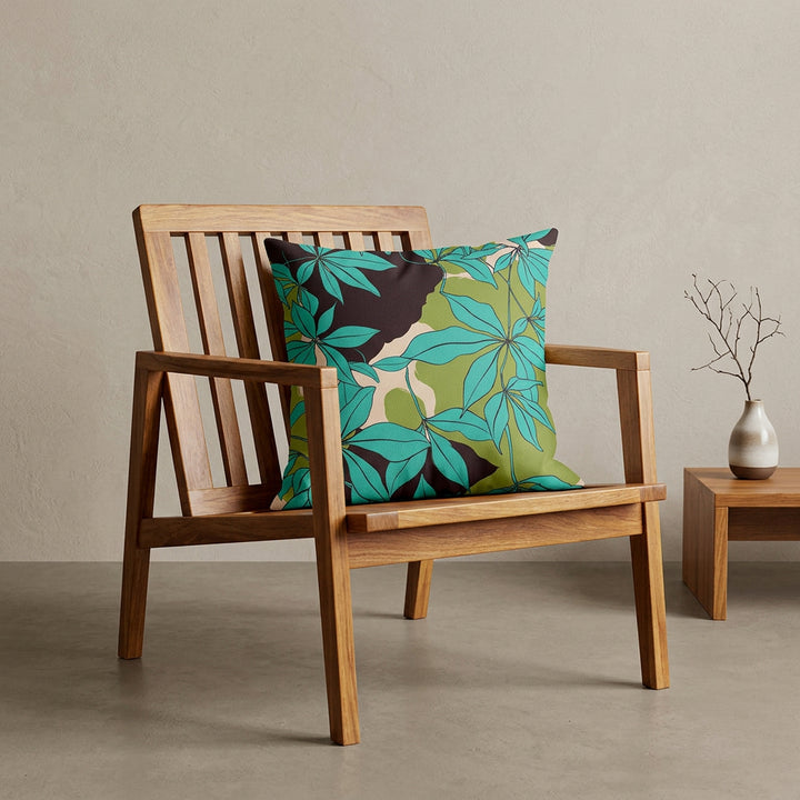Photographie professionnelle extrêmement détaillée et de haute qualité d'un coussin mzelle design motif stylisé feuilles eucalyptus, disposé sur un tabouret japonais moderne en bois d'acacia vernis disposé contre un mur, dans un décor beige neutre, sobre, sol en ciment couleur neutre.