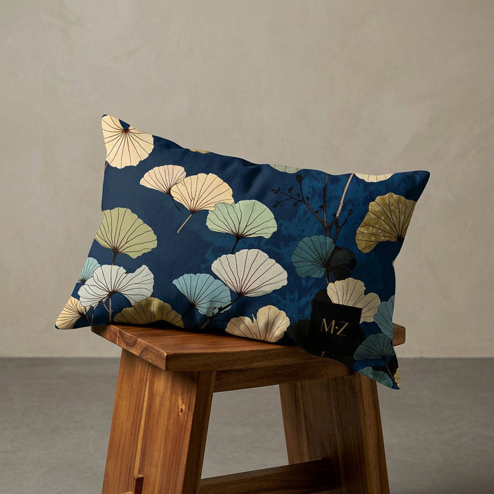 Photographie professionnelle décoration japandi, d'un coussin mzelle design motif ginkgo disposé sur un tabouret japonais moderne en bois d'acacia vernis disposé contre un mur, dans un décor beige neutre, sobre, sol en ciment couleur unie.
