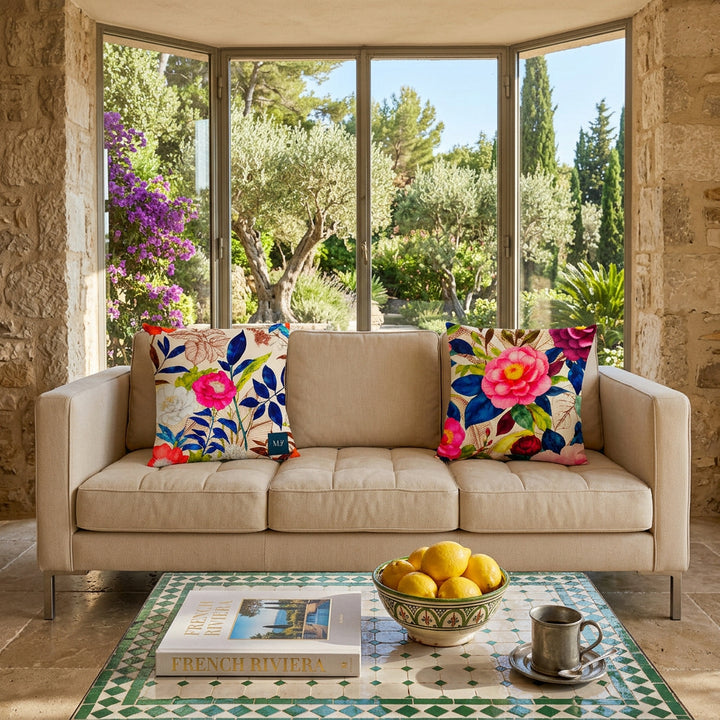 Photo professionnelle de décoration salon d'une villa ambiance french riviera, gros plan de face sur un canapé moderne 3 places, en twill écru, orné de deux coussins mzelle design motifs floral acidulé , devant une alcôve en pierres, sol en pierres, table basse recouverte de mosaiques vert et blanc, ambiance estivale.