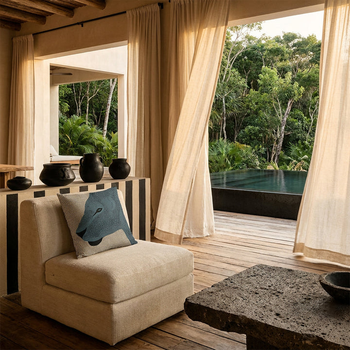 Photo professionnelle lifestyle, décoration terrasse d’eco-lodge tropical haut de gamme, fauteuil en tissu naturel écru texturé orné de d'un coussin mzelle design motif graphique , table basse en pierre volcanique, sol en bois brut, poteries artisanales sur un muret peint de rayures noires, rideaux en lin flottant dans une brise chaude, architecture ouverte sur une jungle luxuriante et piscine sombre moderne.