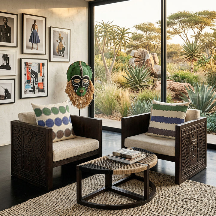 photographie professionnelle, esthétique éditoriale, décoration villa d'architecte en Afrique du sud, deux fauteuil massifs, en wengé sculptés sur les côtés, assises de lin écru, ornée chacun d'un large coussin mzelle design à motifs géométriques, mobilier en bois de wengé foncé, table basse demi line en cordage noir et brut, affiches mode et art urbain sur un pan de mur, tapis berbère texturé sur sol en ciment noir poli, masque Burkinabé en fibres textiles vert et perles.