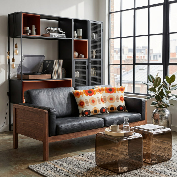 photo de décoration, Grand loft industriel, Mid-Century Modern hybride et éclectique, avec verrière noire style atelier baigné de lumière naturelle, vue de face sur un canapé vintage en cuir noir orné de 2 coussins mzelle design motifs géométriques retro. En arrière plan: Bibliothèque modulaire asymétrique noir mat avec niches orange brûlé en résine, style anciens casiers industriels, une Platine et des vinyles, livre de jazz. 