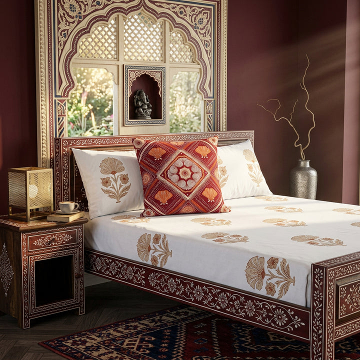 Photographie professionnelle de décoration de chambre Inde, avec un superbe lit Style dravidien, structure en bois de manguier peint à la main de motifs floraux Indien rouges et blanc, orné d'un large coussin mzelle design motif géométrique au centre. Table de chevet en bois de manguier peint à la main et accessoires.