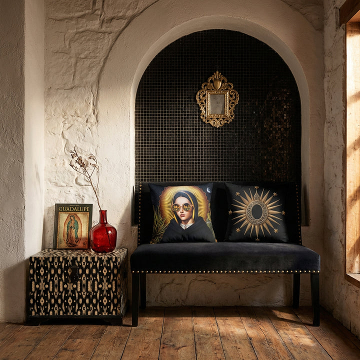 Photographie professionnel décoration intérieure de loft mexicain, banquette de velours noir finitions rivets laiton design moderne, orné de 2 larges coussins carrés mzelle design motif madone et médaillon sacré placé devant une niche en arche de mosaiques noir dans le mur en pierres blanchies, décoré d'un EX VOTO en laiton, coffre peint d'un motif.