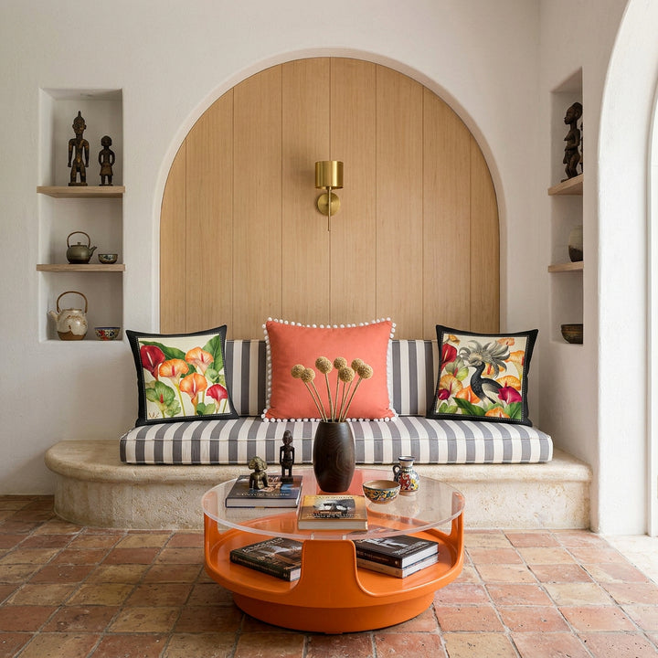 Photo professionnelle de décoration d'intérieur, villa provençale baignée de soleil avec murs blanchis à la chaux,  canapé taillé dans la pierre surélevé sur une marche arrondie, assises à rayures grises et blanc, orné de 2 coussins mzelle design de chaque côté et un coussin corail au centre finitions petits pompons blancs, bibliothèque et objets artisanaux.