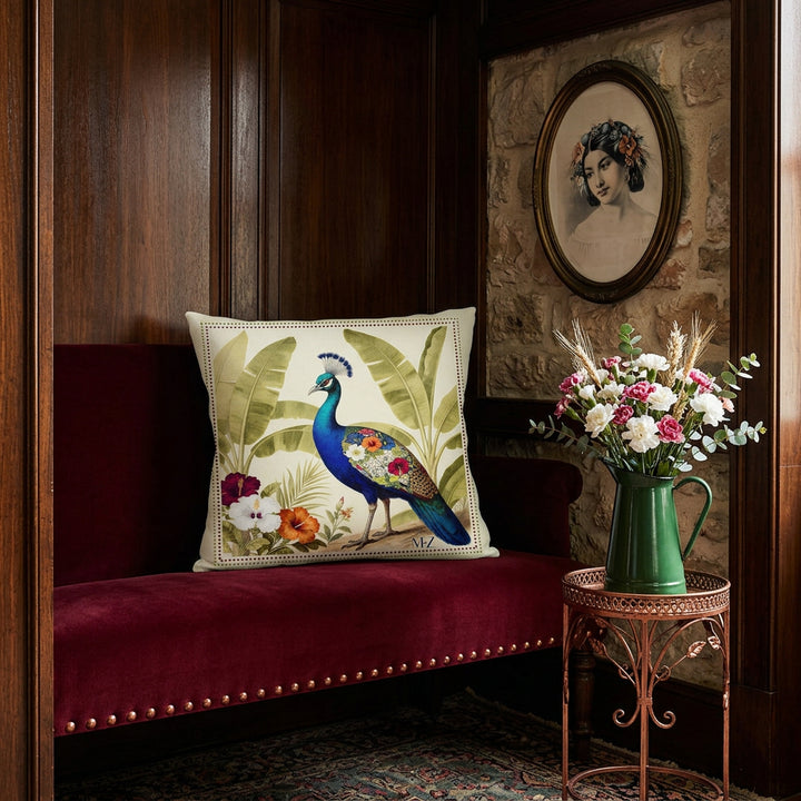 photographie professionnelle, décoration d'un boudoir italien, large coussin carré mzelle design motif paon bleu, posé sur une banquette régence en velours mat rouge grenat, finitions rivets cuivrés, placée dans une alcôve en bois clair verni. Mur en pierre, portrait lithographie de femme créole, sur un guéridon en fer forgé cuivré un bouquet d'oeillets blancs et rose dans un broc en émail vert foncé.