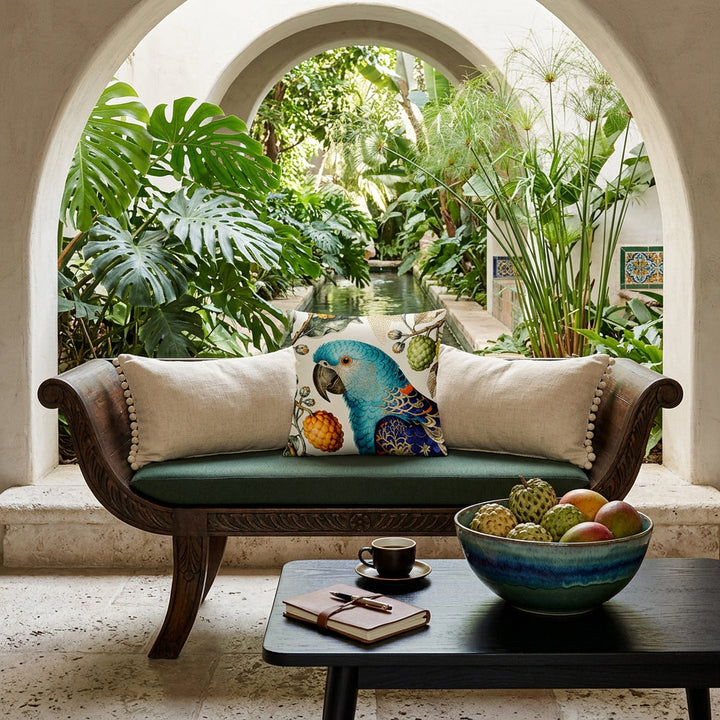 photographie professionnelle d'un intérieur cottage tropicale, une banquette de bois noir orné d'un large cousin mzelle design motif perroquet bleu,  et de coussins rectangle à petits pompons écrus de chaque côté. Table basse en bois noir avec une tasse de café, carnet, coupe en grès bleu dégradé contenant des attiers et des mangues. En arrière plan, une arche ouverte sur un jardin espagnol.