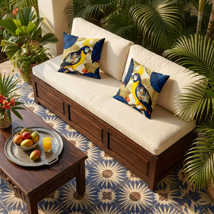 Photo professionnelle lifestyle, décoration estivale, villa au costa-rica, vue en plongée sur une banquette-coffre en bois de wengé verni et assises écrues en lin, ornée de deux coussins mzelle design motif perroquets, sol en carrelage bleu indigo, écru et brun formant un soleil, table en wengé  garnie d'un plateau en étain avec une coupe de fruits tropicaux (mangues et attiers) et un verre de jus de fruit.