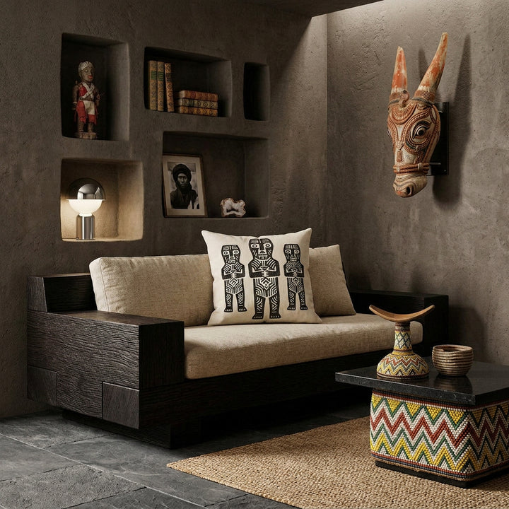 Photo professionnelle de décoration d'intérieur, salon afro chic brutaliste, vue de face. Canapé sculptural bas en bois de wengé massif aux lignes géométriques monolithiques, assises tissu texturé sable, orné d'un large coussin mzelle design, motifs tribaux. Murs en béton brut teinté argile sombre, niches architecturales asymétriques intégrées exposant divers objets décoratifs et masque bovin africain. 