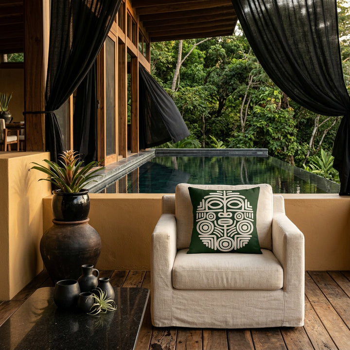 Photo professionnelle lifestyle, décoration terrasse d’eco-lodge du costa-rica, grand fauteuil en tissu crème texturé vue de face, orné d'un large coussin mzelle design motif masque maya , table basse en pierre volcanique, sol en bois brut, poteries artisanales dans un muret peint en ocre, rideaux en lin noir flottant dans une brise chaude, architecture ouverte sur une jungle luxuriante et piscine. 