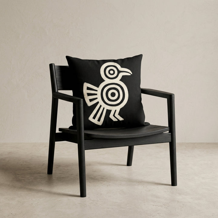 Photographie professionnelle studio, décoration avec un coussin mzelle design motif maya disposé sur un fauteuil japandi moderne en bois noir vernis, assise en bois, disposé contre un mur, dans un décor beige neutre, sobre.