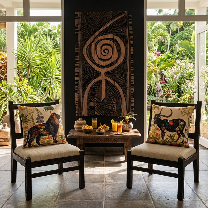 Photo professionnelle de décoration d'intérieur, salon Arty, villa créole. Au premier plan vue de face de 2 chaises style tribale  en bois wengé rustiques, assises en twill écru chacune ornée d'un coussin mzelle design motif jungle. Mur peint en noir décoré d'un grand panneau en bois,  table basse bois brut wengé sculptée, garnie de tapas et 2 verres de jus de fruit. Carrelage rustique gris minéral, ouverture sur un jardin tropicalisé