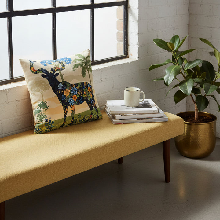 Photographie d’intérieur décoration de loft boho chic, vue en plongée en gros plan sur une banquette en tissu lin jaune paille orné d'un coussin mzelle design motif animalier, adossé au mur sous une fenêtre industrielle, à côté d'une tasse de café en céramique émail mat posée sur une pile de livres d'art, ficus dans un pot en laiton sur le sol, mur blanchi en vieilles pierres.