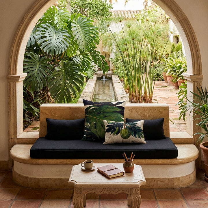 photographie professionnelle d'une  hacienda tropicale, banquette de pierre surélevé sur une marche arrondie, orné de 2 coussins mzelle design motifs tropical. Table basse assortie avec une tasse de café, carnet, pot à crayons. En arrière plan, une arche ouverte sur un jardin espagnol. 