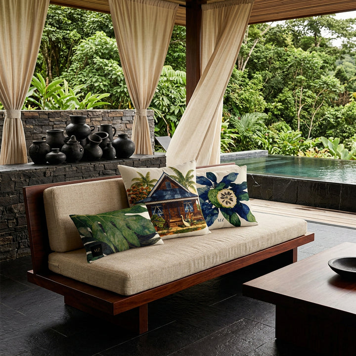 Photo professionnelle lifestyle, décoration terrasse d’eco-lodge du costa-rica, banquette moderne bois de mahogany orné de trois coussins mzelle design motif maison créole et oiseau, table basse assortie, sol en carrelage noir, poteries artisanales empilées de façon artistique dans un muret , rideaux en lin crème flottant , architecture ouverte sur une jungle luxuriante et piscine sombre moderne.